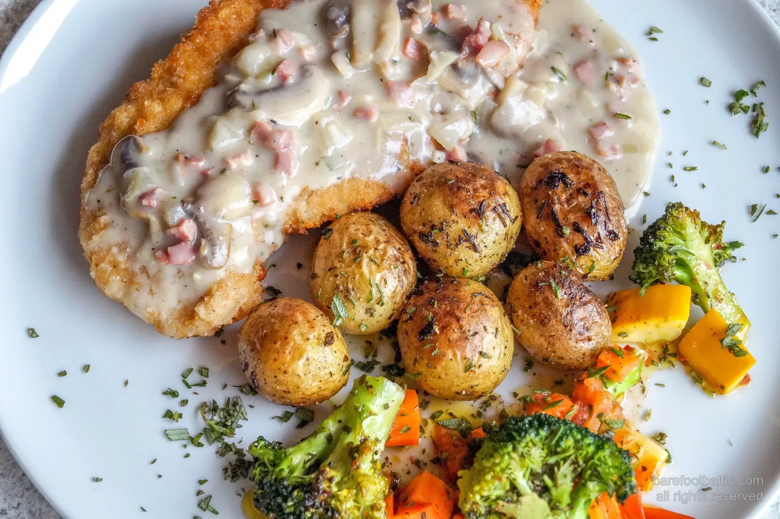 A plate of karbonāde — Latvian breaded pork cutlet — with creamy mushroom sauce, herbed potatoes and roasted vegetables